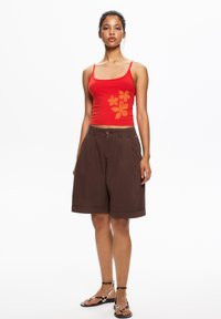 Red tank top with orange floral print, paired with brown knee-length shorts, and black and white strappy sandals. Smooth fabric, casual design.