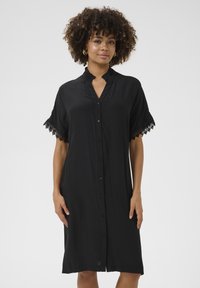 Melna pogu krekla kleita ar apmali un īsām piedurknēm. Mežģīņu apdare piedurkņu maliņās; gaisīga auduma ar brīvu piegriezumu.