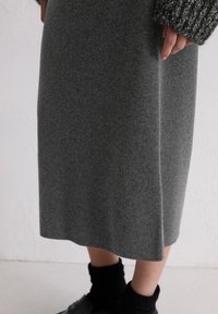Jupe midi en mélange de laine gris avec une texture douce, une silhouette droite et des détails discrets sur les coutures latérales, associée à des chaussettes en tricot noires et des chaussures.