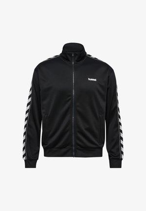 Schwarze Trainingsjacke mit Reißverschluss, weiße Chevron-Streifen entlang der Ärmel und kleines weißes "hummel"-Logo auf der linken Brust.