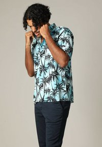 Korte mouwen overhemd met knopen in lichtblauw met zwart palmboomprint, voorzien van een kraag en een relaxte pasvorm, gedragen met donkere broeken.