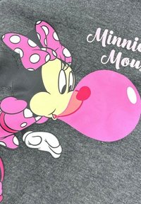 Un tissu gris présente un graphique d'un personnage de dessin animé avec un visage noir et jaune, un nœud papillon rose à pois, une robe rose, en train de souffler une grande bulle rose.