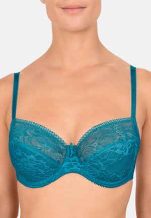 Sottoveste in pizzo teal con coppe a supporto, decorata con motivi floreali, dettaglio a fiocco al centro e spalline regolabili con bordi a scalloped. Texture del tessuto liscia.