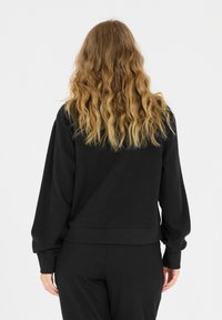 Schwarzer, gerippter Sweatshirt mit lockerer Passform, weiten Ärmeln und einem gerippten Saum. Die Textur wirkt weich und leicht dehnbar.