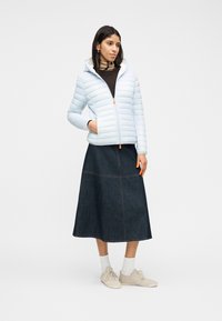 Γυναίκα που φοράει ανοιχτό μπλε μπουφάν puffer, midi φούστα από σκούρο τζιν, μπεζ αθλητικά παπούτσια, λευκές κάλτσες και ριγέ ζιβάγκο πουλόβερ σε μπεζ και καφέ αποχρώσεις.