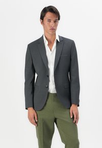 Grau maßgeschneiderter Blazer mit Reverskragen, zwei Knöpfen, Taschen vorne und schmaler Passform, kombiniert mit einem weißen Hemd und grünen Hosen.