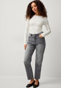 Leichter, langärmliger weißer Body, kombiniert mit hoch taillierten grauen Jeans. Die Jeans haben einen geraden Schnitt und ein klassisches Fünf-Taschen-Design.