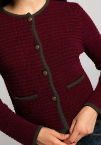 Cárdigan de punto en burdeos con patrón texturizado, ribete verde, escote redondo y dos bolsillos frontales. Presenta botones decorativos de latón.