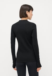 Svart langermet topp med en tettsittende design, rund halslinning og tommelholdere ved mansjettene. Glatt tekstur med subtile sømdetaljer.