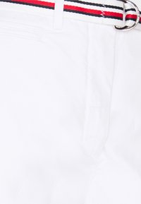 Pantaloni corti bianchi con tasche laterali, dotati di una cintura a strisce multicolori in rosso, nero e bianco, con un dettagli di fibbia argentata.