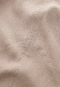 Vaaleanbeige-pellavakangas, jossa on sileä pinta, sisältäen hienovaraisia, epäsäännöllisiä kudoksia ja pieniä ryppyjä, jotka korostavat ommeltuja yksityiskohtia.