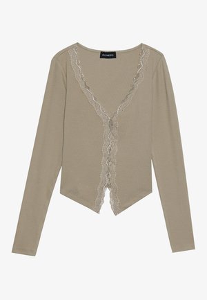 Top beige à manches longues avec un décolleté en V, présentant des bords en dentelle festonnée et un design de bas arrondi et court.