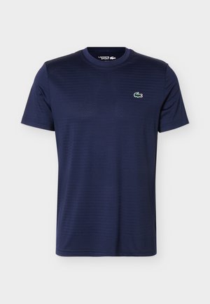 Tumesinise värviga lühikeste varrukatega spordisärk ümarsärgkaelusega, millel vasakul rinnal väike roheline ja valge krokodillilogoga.