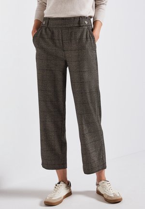 Personne portant un pantalon à carreaux taille haute et jambes larges avec des poches latérales, associé à des baskets blanches et un haut beige à manches longues.