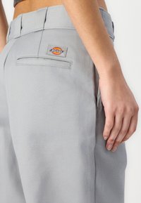 Hallid hallid Dickies püksid on otsekesega ning tagaküljel on pilt õmmeldud logoga tasku. Kangas näeb välja vastupidav ja selle tekstuur on sile.