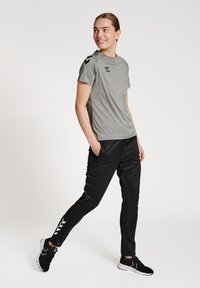 Grå kortærmet sports T-shirt med sort logo, parret med sorte bukser med sidelommer og hvide chevron-accenter. Sorte atletiske sko.