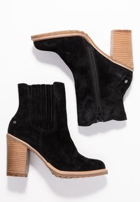 Botines de ante negros con diseño acanalado, cremallera lateral y tacón de madera apilada. Cuenta con una suela-texturizada para mayor tracción.