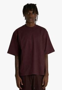 Maglietta oversize color borgogna in cotone con scollo rotondo e maniche corte. Tessuto liscio, vestibilità rilassata, design minimalista.