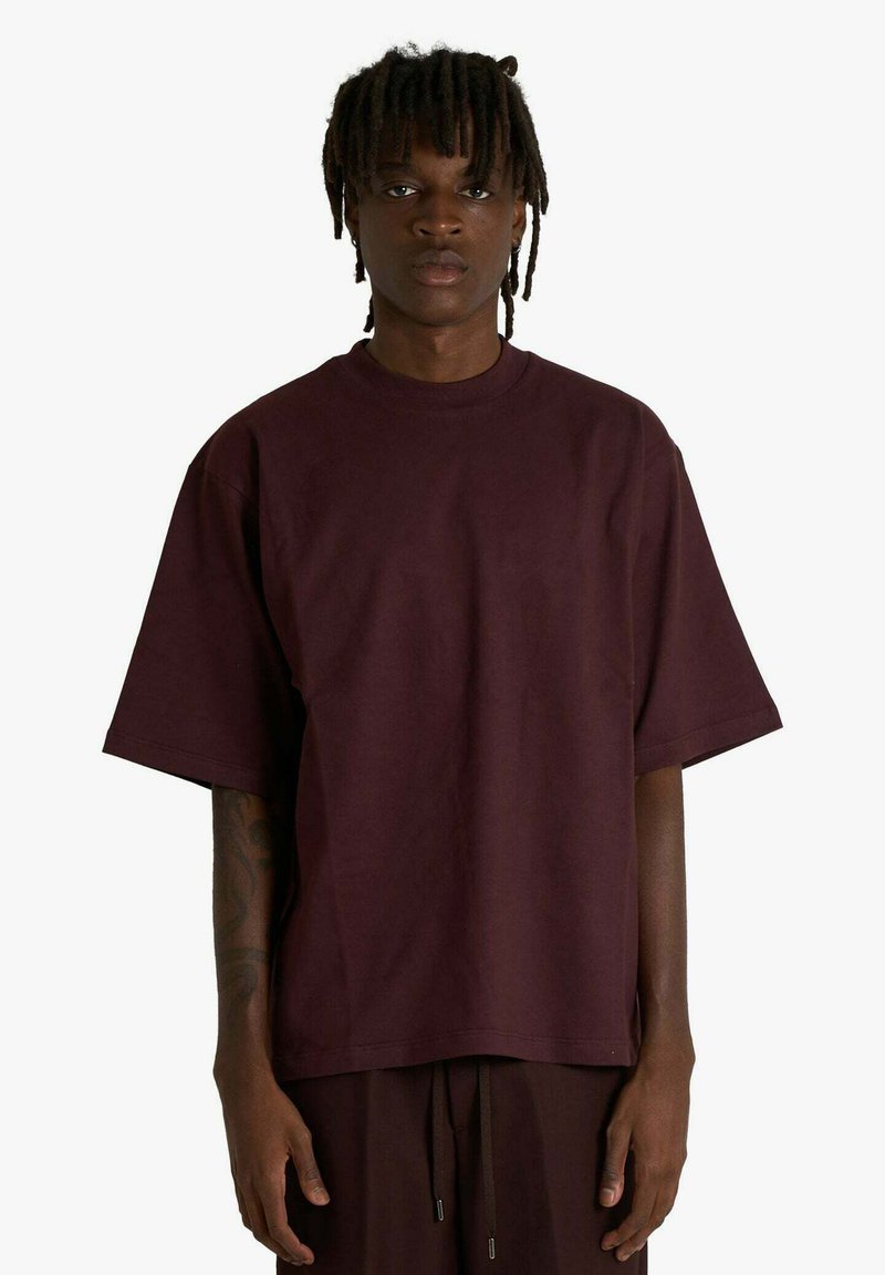 Maglietta oversize color borgogna in cotone con scollo rotondo e maniche corte. Tessuto liscio, vestibilità rilassata, design minimalista.