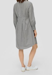 Robe rayée gris et blanc, à manches longues, taille cintrée et jupe évasée. Stylée avec des baskets blanches, tissu texturé.