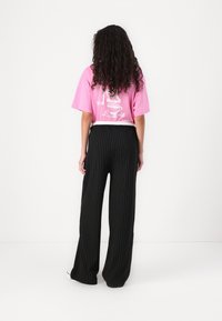 T-shirt graphique rose à coupe décontractée et manches courtes, associé à un pantalon noir à rayures verticales taille haute, au design large.