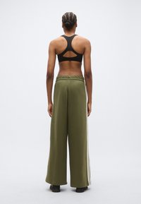 Czarny sportowy biustonosz z wycięciem na plecach; luźne, oliwkowozielone spodnie dresowe z bocznymi paskami i elastycznym pasem.