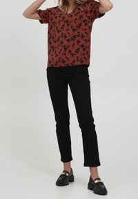 Haut rouge à manches courtes avec un motif floral noir, associé à un pantalon noir ajusté et des chaussures noires avec des accents dorés.