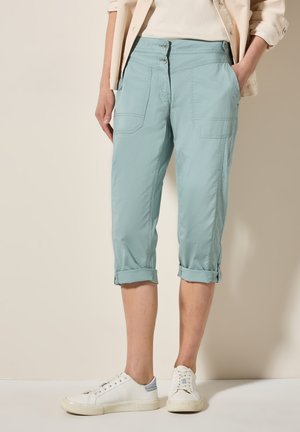 Pantalones cortos de color azul claro con dobladillos acabados, dos bolsillos frontales y dos cierres de botón en la parte delantera. Combinados con zapatillas blancas. Textura suave.
