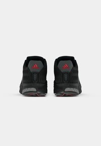 Baskets de sport noires avec un dessus en maille texturée, accents rouges et talon rembourré. Caractéristiques d'une semelle en caoutchouc avec un motif de traction distinct.
