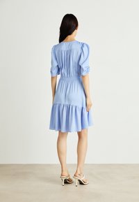 Vaaleansininen mekko puffihihnoilla, kootulla vyötäröllä ja kerroksellisella helmalla. Valmistettu sileästä kankaasta, jossa on hienovarainen tekstuuri ja lentävä muotoilu.