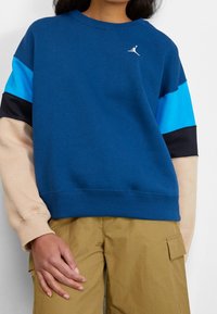 Felpa blu con maniche a blocchi di colore in azzurro, nero e beige. Presenta una scollatura a girocollo e un piccolo logo sul petto.