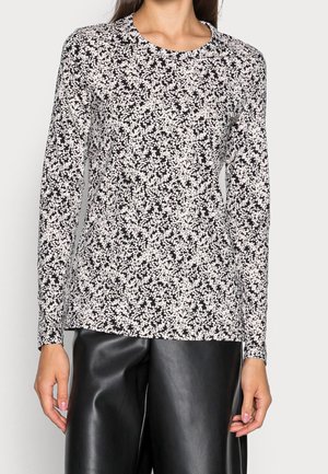Femme portant une chemise noire et blanche à manches longues à motif floral, associée à un pantalon en cuir noir, visible du cou jusqu'au milieu de la cuisse.