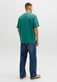 Groen katoenen T-shirt met een ronde hals, korte mouwen en een losse pasvorm, gecombineerd met losse blauwe spijkerbroek en beige schoenen.