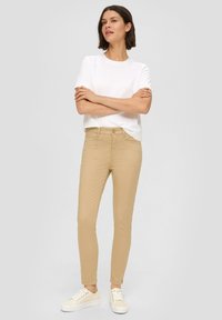 Hlače do kolen, prilegajoče se, v bež barvi z srednjim pasom, sprednjimi žepi in subtilno teksturo, v kombinaciji s preprosto belo majico in supergami.