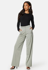 Maglietta a maniche lunghe nera a costine abbinata a pantaloni larghi verde chiaro con tasche laterali. La modella indossa sandali neri con tacco.