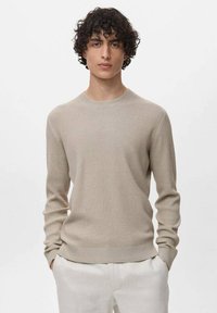 Maglione a coste beige con scollatura rotonda e maniche lunghe. Presenta un punto vita aderente e un motivo testurizzato su tutta la superficie.