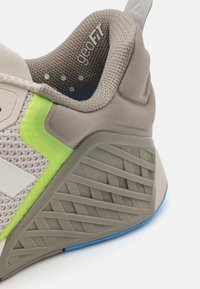 Gray sneaker with a textured design, featuring a lime green accent, padded collar, and a patterned rubber sole with blue detailing.
