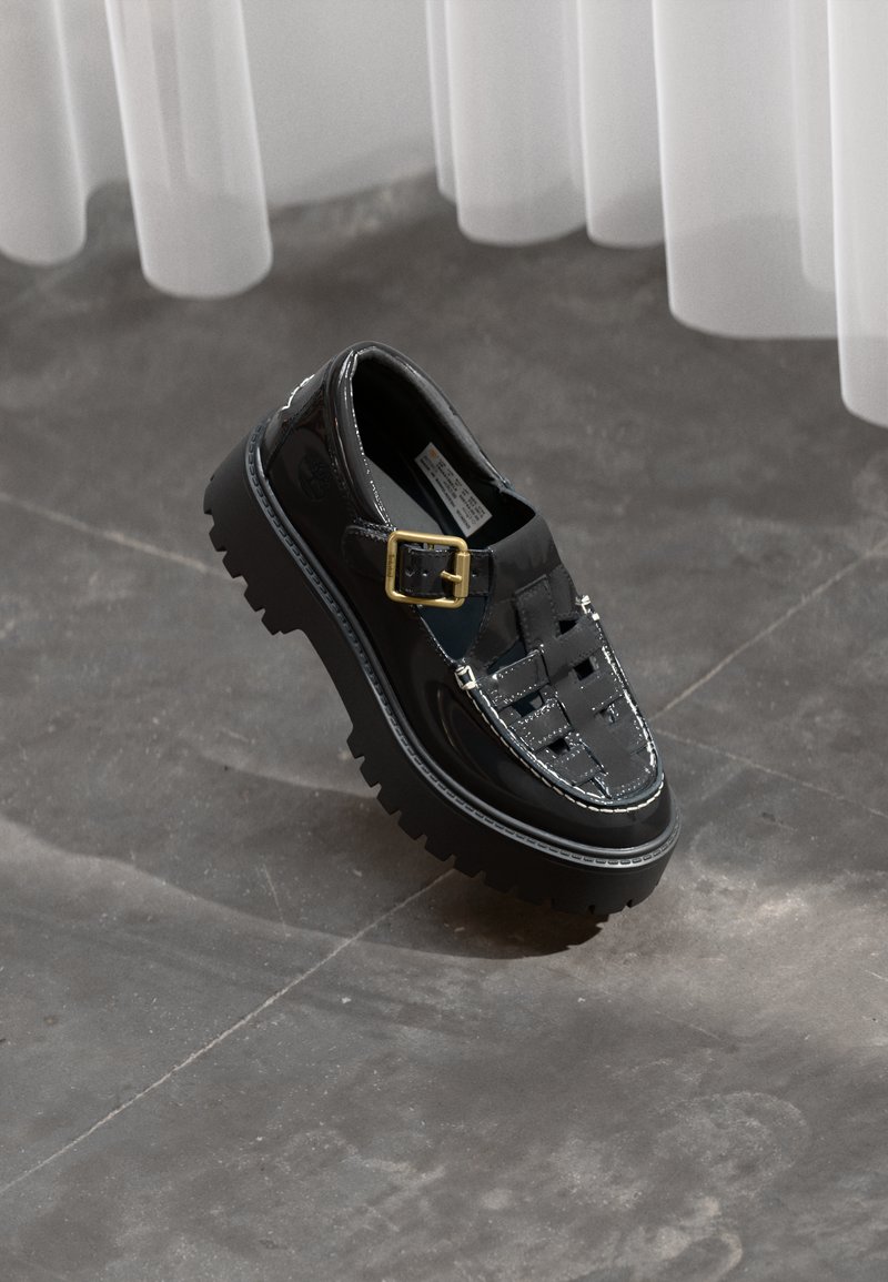 Sapatos de verniz preto com um design trançado e uma fivela dourada, apresentando uma sola chunky e detalhes de costura branca em contraste.