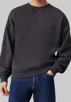 Felpa grigia scura realizzata in un materiale morbido, con collo rotondo, spalle scese, polsini e orlo a costine, dal design ampio.