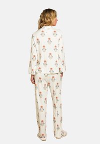 Lange mouw pyjama set in romige stof, met een bloemenpatroon van oranje en blauwe bloemen. Zachte textuur, ontspannen pasvorm en rechte broekspijpen.