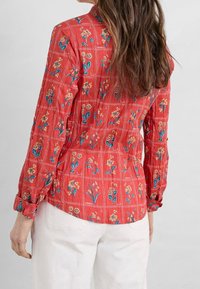 Rode blouse met een bloemenpatroon, met blauwe en gele accenten. Lange mouwen met knoopmanchetten, textiel met een structuur.