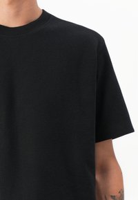 Camisa negra de manga corta fabricada con un tejido texturizado, con escote redondo y corte relajado. Sin patrones visibles ni detalles de hardware.