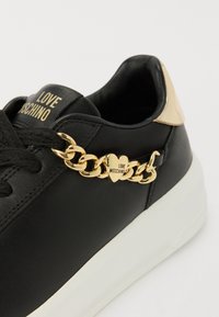 Black leather sneaker featuring a gold chain accent with a heart detail, a white sole, and "LOVE MOSCHINO" branding on the tongue.