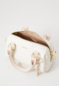 Weißes Handtasche mit geometrischem Muster, zarten rosa Akzenten, goldenen Beschlägen, doppelten Griffen und einem oberen Reißverschluss. Innenbeutel ist beige.