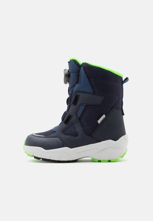 Botte d'hiver enfant bleu marine avec doublure vert vif, semelle blanche et semelle noire, équipée d'un cadran et de bandes Velcro pour la fixation.