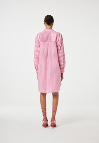 Gestreiftes Kleid in Pink und Weiß, leichtes Material, lange Ärmel, mit Knöpfen versehen und einem Rückenschlitz, kombiniert mit pinken Riemchen-Heels.