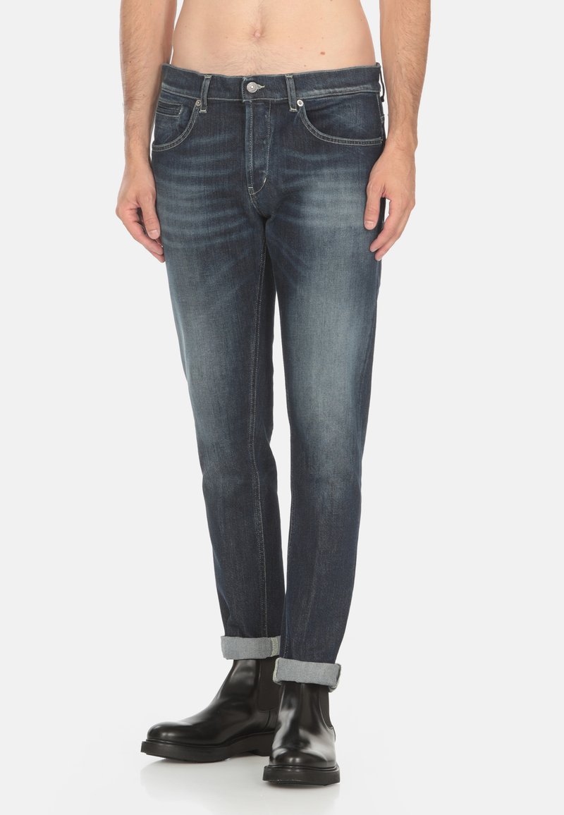 Jeans in denim blu slim-fit con effetti di scoloritura e whiskering. Presenta cinque tasche, chiusura a bottone e orli arrotolati. Abbinati a stivaletti neri.