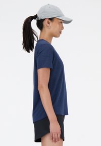 Ναυτικό μπλε αθλητικό μπλουζάκι κοντομάνικο, κατασκευασμένο από υφασμάτινη δομή, εύκολα συνδυασμένο με μαύρες βερμούδες, φορεμένο με ελαφρύ γκρι καπέλο.