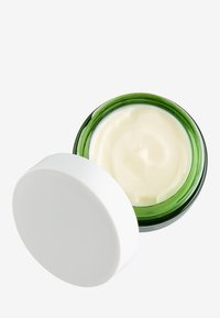 Grön glasburk som innehåller en krämig vit fuktighetskräm med ett vitt lock. Slät textur synlig inuti burken.