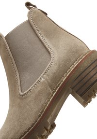 Stivaletto Chelsea in suede marrone con pannelli laterali elasticizzati, tacco basso e suola in gomma testurizzata con righe verticali.
